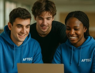 trois jeunes devant un écran et souriant. celui de gauche et l'étudiante de droite portent tous les deux un sweat AFTEC bleu. l'étudiant du milieu porte un t-shirt noir basique. les deux jeunes à gauche ont la peau blanche et la jeune à droite à la peau de couleur noir