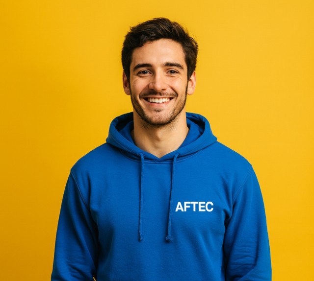 jeune homme de 24 ans portant un sweat à capuche bleu avec le logo AFTEC sur un fond jaune uni