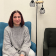 Photo de Jennyfer, étudiante en BTS Tourisme, elle est assise au sein des locaux AFTEC, porte un pull en laine, a les cheveux courts et sourie.