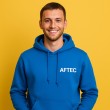 photo d'un alumni de l'école AFTEC, il porte un sweat bleu à capuche avec le logo AFTEC, sur un fond jaune