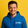 photo d'un alumni de l'école AFTEC, il porte un sweat bleu à capuche avec le logo AFTEC, sur un fond jaune